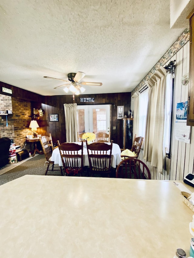 dining area with a textured ceiling, ceiling fan, and wood walls