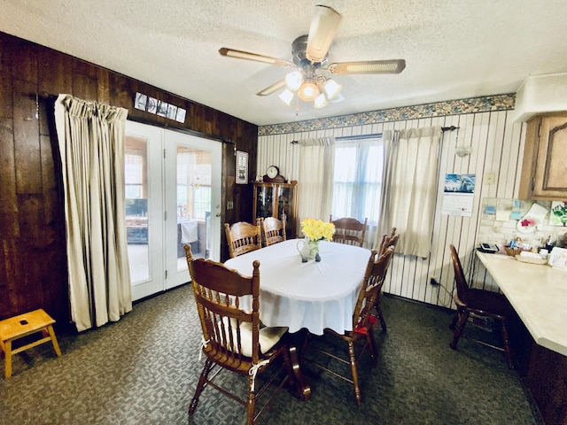 dining room featuring wooden walls, a textured ceiling, ceiling fan, and dark colored carpet