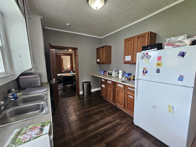 kitchen featuring dark wood-style flooring, brown cabinetry, light countertops, ornamental molding, and freestanding refrigerator