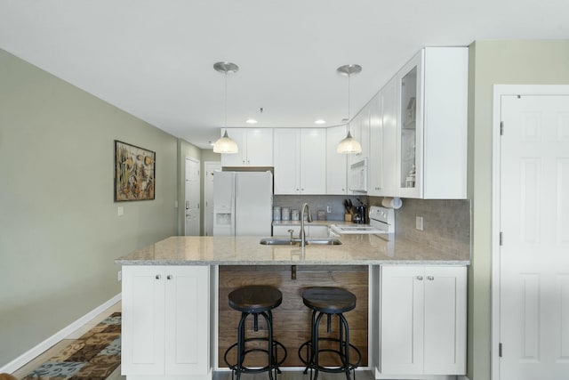 kitchen featuring a sink, white appliances, a peninsula, baseboards, and white cabinets