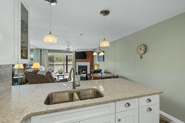 kitchen with white cabinets, decorative backsplash, a lit fireplace, and a sink