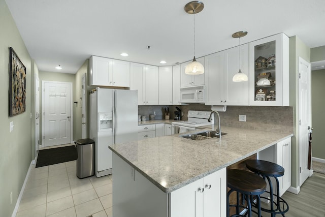 kitchen featuring baseboards, white appliances, a peninsula, and light stone counters