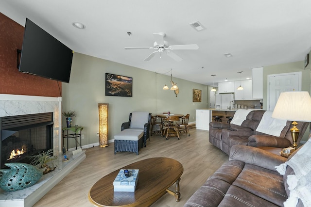 living room with a premium fireplace, light wood-style floors, a ceiling fan, visible vents, and baseboards