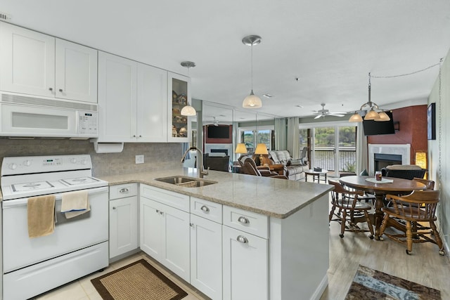 kitchen with a sink, a fireplace, a peninsula, white appliances, and white cabinets