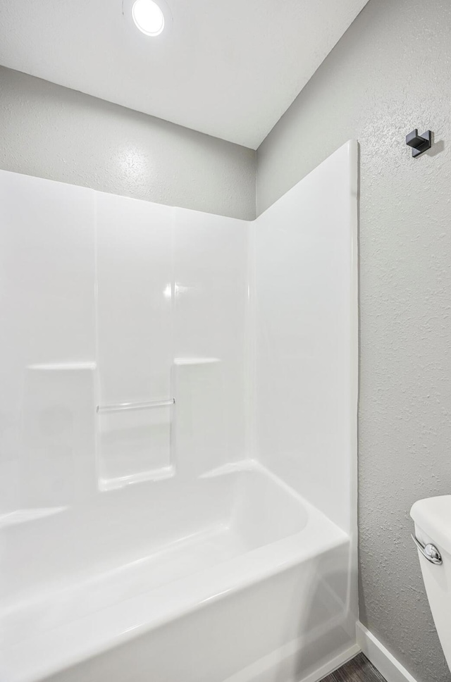 full bathroom with wood finished floors, a bathing tub, toilet, a textured wall, and baseboards