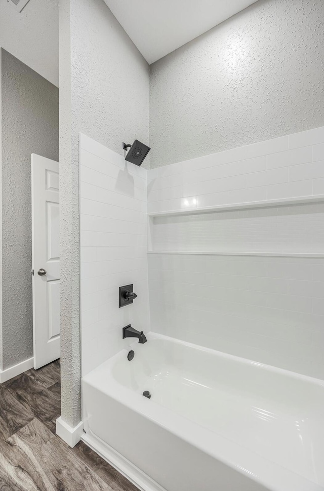bathroom featuring a textured wall, bathing tub / shower combination, wood finished floors, and baseboards