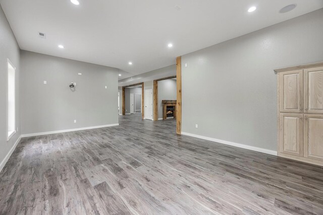 unfurnished living room featuring a warm lit fireplace, recessed lighting, wood finished floors, and baseboards