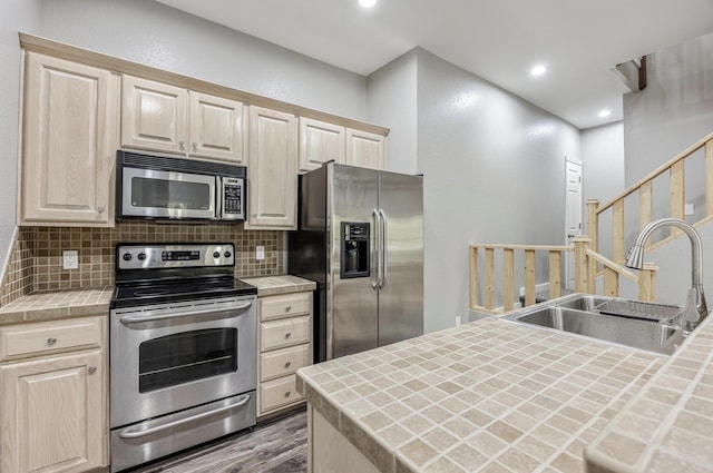 kitchen featuring appliances with stainless steel finishes, a sink, light brown cabinets, and tile countertops
