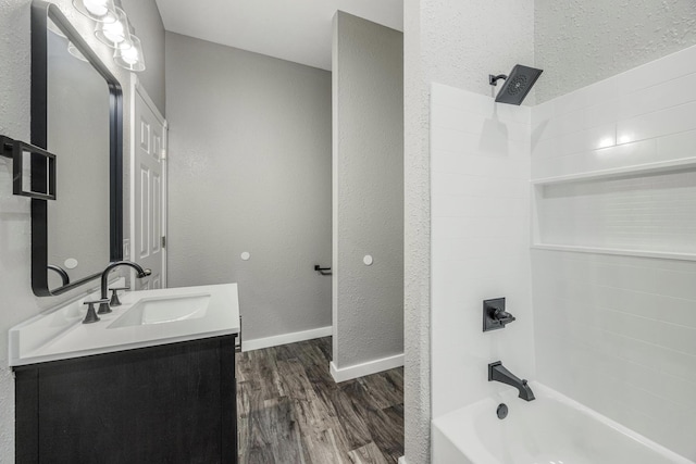 bathroom featuring vanity, a textured wall, baseboards, wood finished floors, and  shower combination