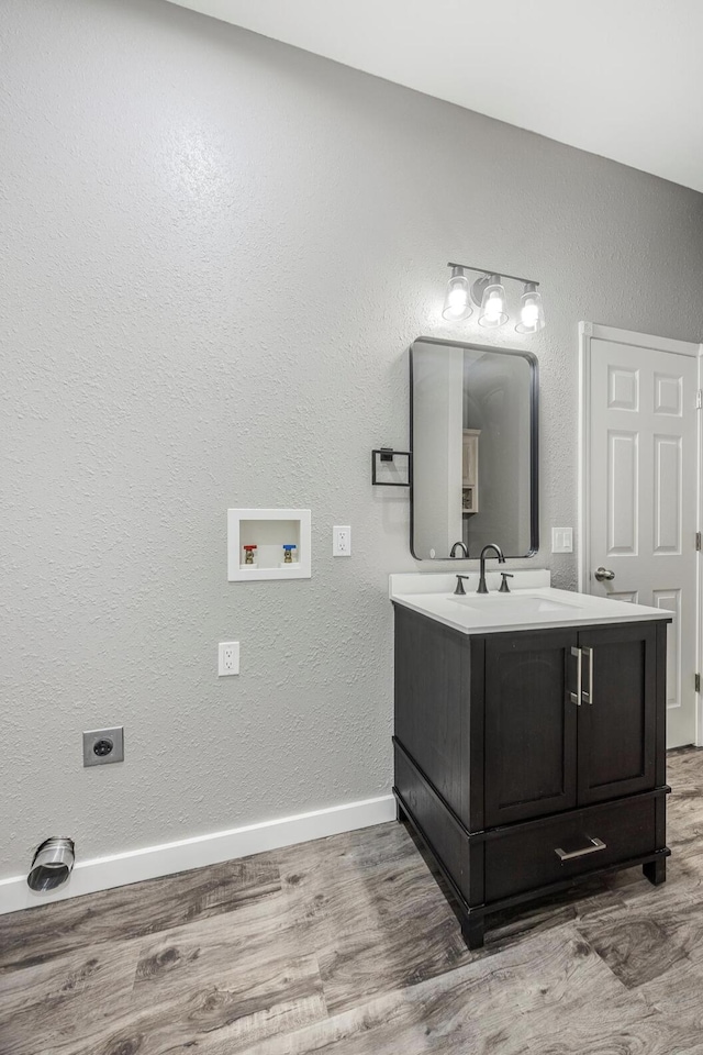 bathroom with vanity, a textured wall, wood finished floors, and baseboards