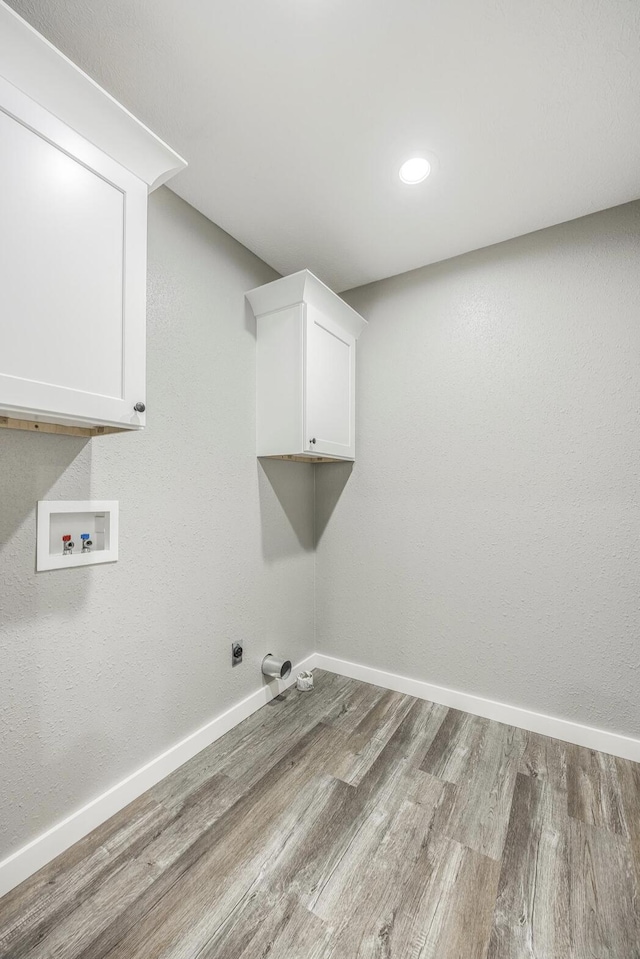 clothes washing area with hookup for a washing machine, cabinet space, wood finished floors, and baseboards