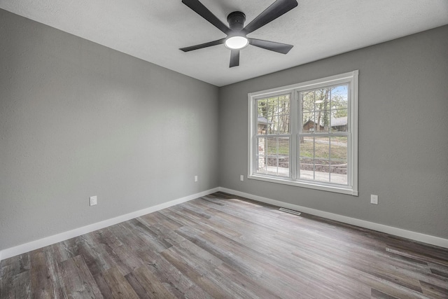 unfurnished room featuring baseboards, visible vents, wood finished floors, and a ceiling fan