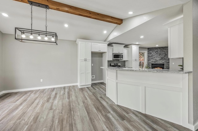 kitchen with light stone counters, white cabinetry, light wood-style floors, stainless steel appliances, and vaulted ceiling with beams