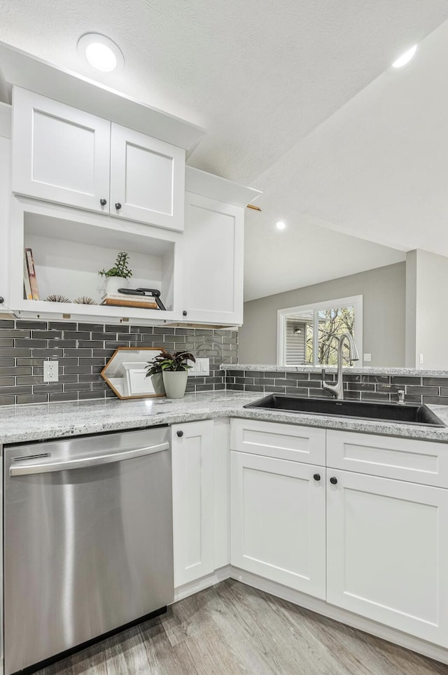 kitchen featuring tasteful backsplash, stainless steel dishwasher, white cabinets, light wood-style flooring, and a sink