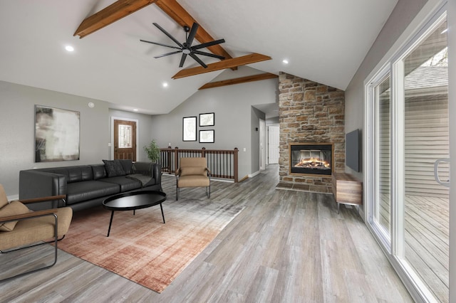 living area featuring beam ceiling, ceiling fan, high vaulted ceiling, a stone fireplace, and wood finished floors