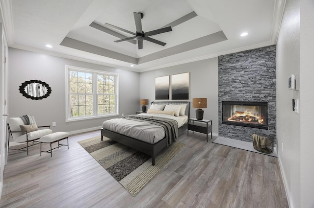 bedroom featuring crown molding, a tray ceiling, baseboards, a fireplace, and wood finished floors