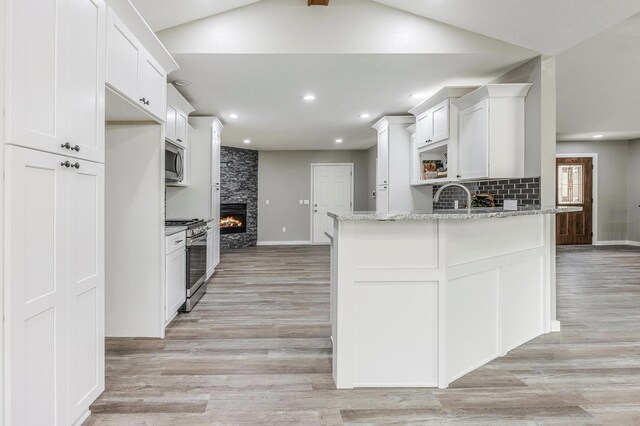 kitchen with light wood-type flooring, white cabinets, stainless steel appliances, and a large fireplace