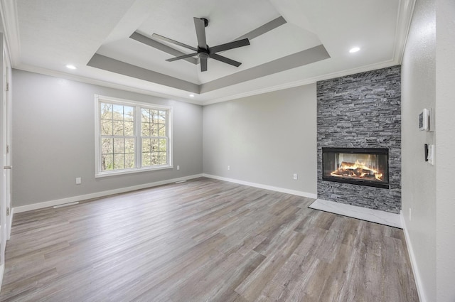 unfurnished living room featuring a tray ceiling, a ceiling fan, a stone fireplace, ornamental molding, and wood finished floors