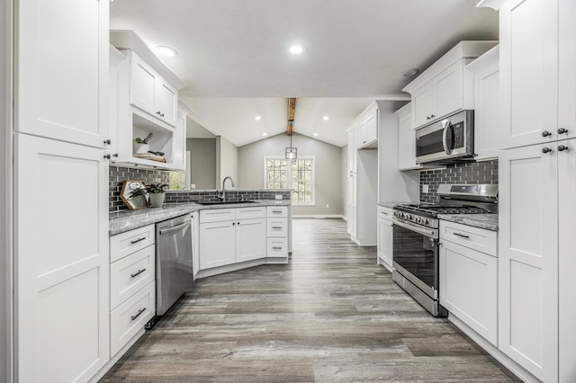 kitchen with vaulted ceiling with beams, appliances with stainless steel finishes, a sink, baseboards, and a peninsula