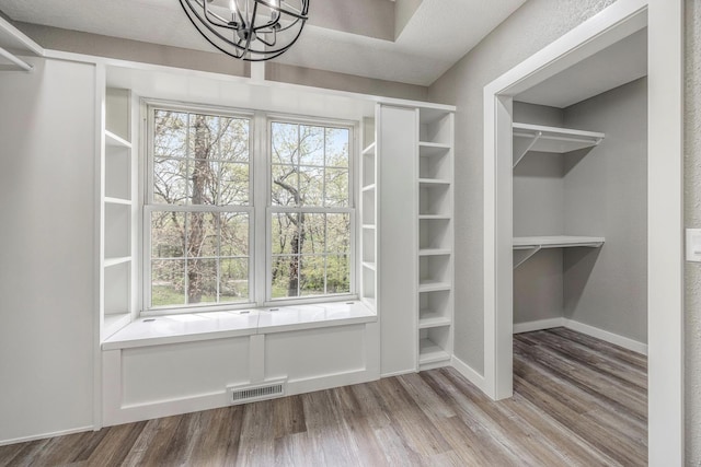 interior space with a chandelier, visible vents, wood finished floors, and baseboards