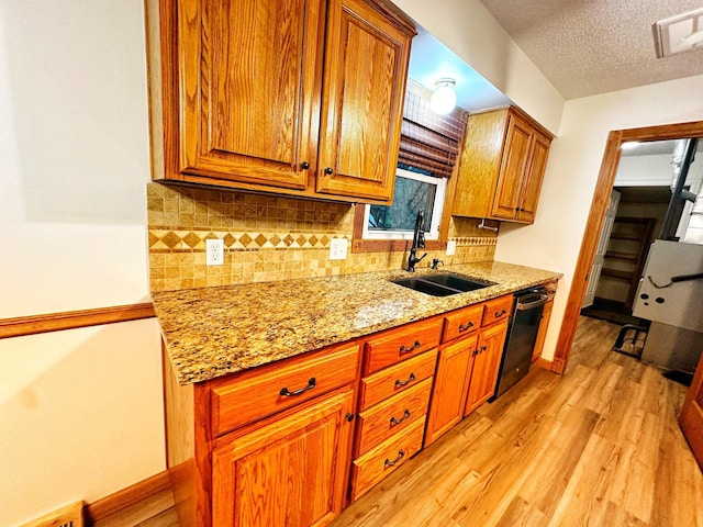 kitchen with decorative backsplash, light wood-style floors, brown cabinets, a sink, and dishwashing machine