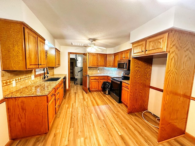 kitchen featuring light wood-style floors, appliances with stainless steel finishes, brown cabinets, a sink, and a ceiling fan