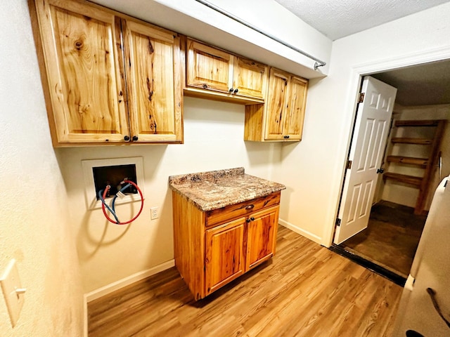 washroom featuring hookup for a washing machine, cabinet space, light wood-style floors, baseboards, and a textured ceiling