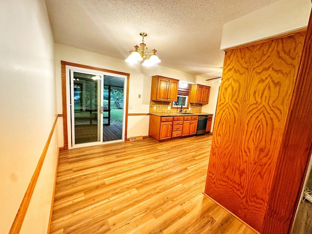 kitchen with a sink, a chandelier, brown cabinetry, light wood-type flooring, and dishwashing machine