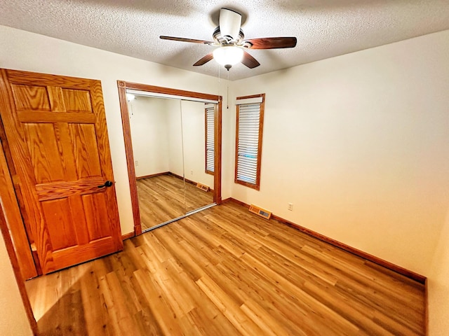 unfurnished bedroom featuring a textured ceiling, light wood-type flooring, baseboards, and a closet