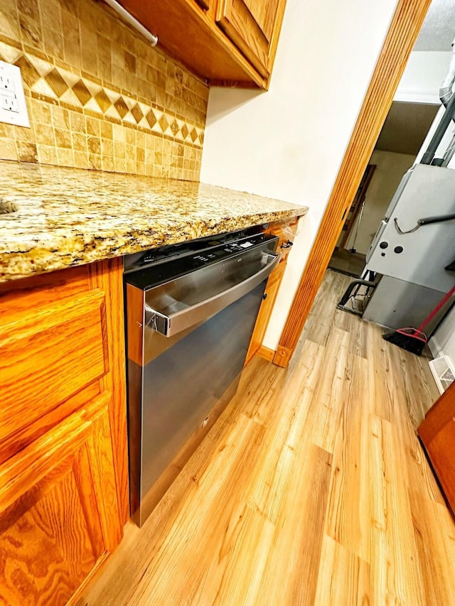 interior details with brown cabinets, decorative backsplash, light wood-style floors, light stone countertops, and dishwasher