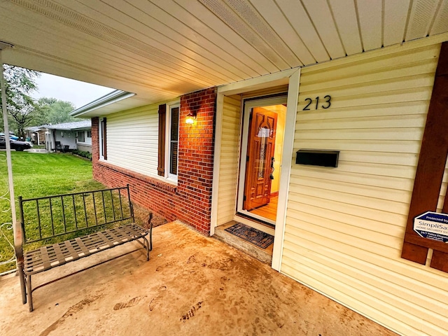 property entrance with a porch, a yard, and brick siding
