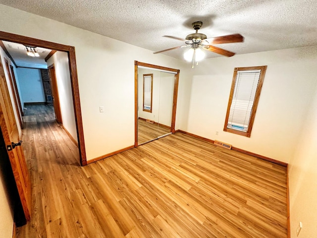 unfurnished bedroom featuring a textured ceiling, visible vents, baseboards, a closet, and light wood finished floors