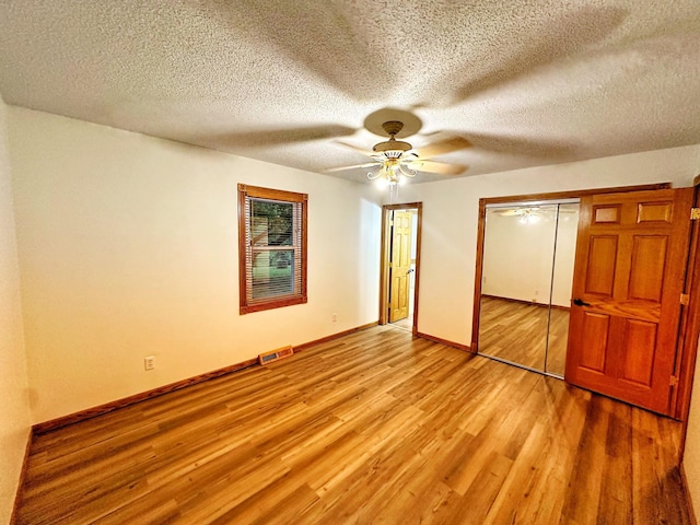 unfurnished bedroom with a textured ceiling, light wood-style flooring, visible vents, ceiling fan, and baseboards