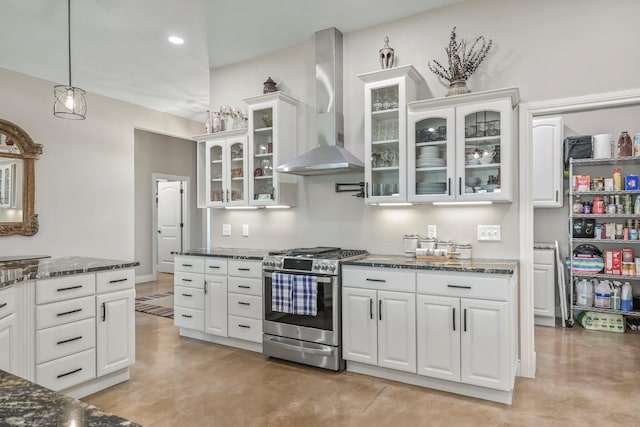 kitchen with wall chimney exhaust hood, dark stone countertops, white cabinets, and gas range