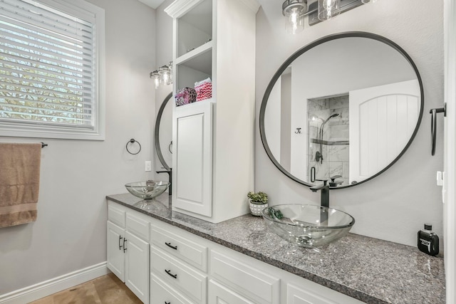 full bathroom with double vanity, a sink, a shower stall, and baseboards