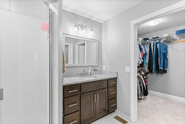 bathroom featuring baseboards, visible vents, a spacious closet, and vanity