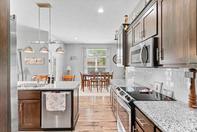 kitchen with tasteful backsplash, light stone countertops, light wood-style flooring, stainless steel appliances, and a sink