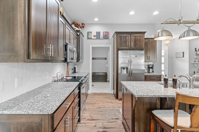 kitchen with appliances with stainless steel finishes, a breakfast bar area, decorative backsplash, and light wood-style flooring
