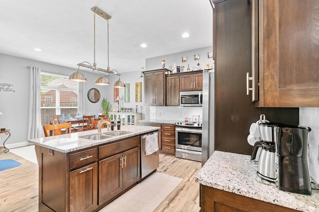 kitchen featuring an island with sink, decorative backsplash, stainless steel appliances, light wood finished floors, and a sink