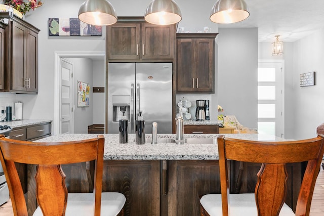 kitchen featuring a breakfast bar area, dark brown cabinets, and stainless steel fridge with ice dispenser