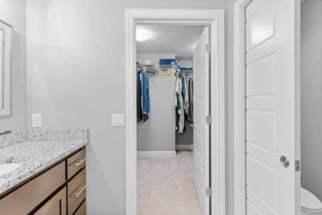 bathroom with vanity, toilet, baseboards, a textured ceiling, and a spacious closet