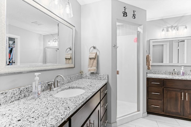 full bath with a walk in closet, two vanities, a stall shower, and a sink