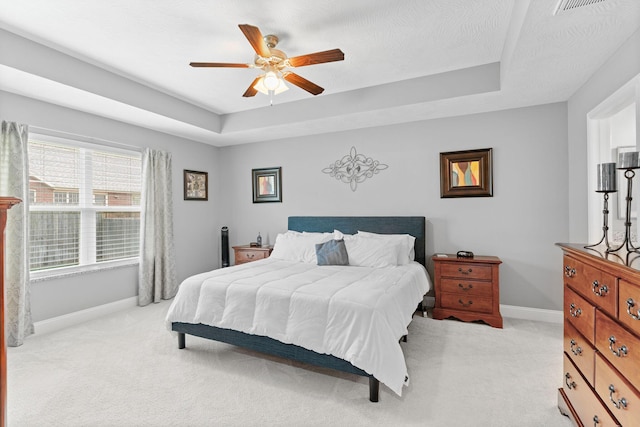 bedroom with light colored carpet, ceiling fan, a tray ceiling, and baseboards