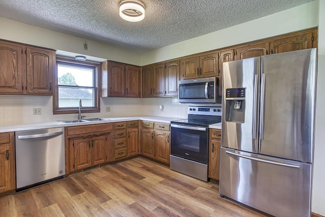 kitchen with a textured ceiling, a sink, appliances with stainless steel finishes, light countertops, and dark wood-type flooring