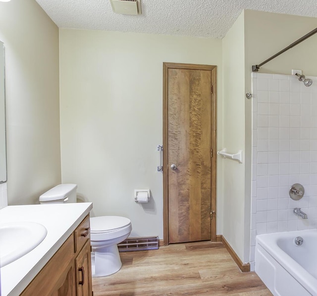 bathroom with wood finished floors, toilet, shower / bathtub combination, vanity, and a textured ceiling