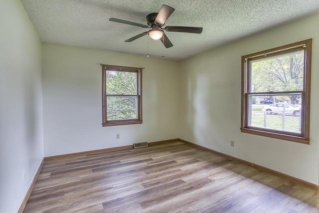 empty room featuring a textured ceiling, visible vents, a ceiling fan, and wood finished floors