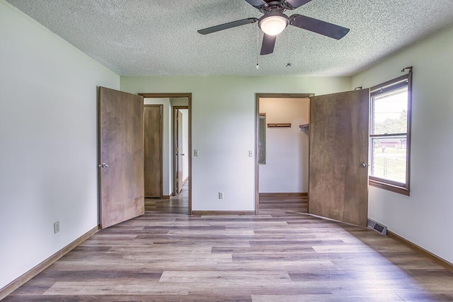 unfurnished bedroom with a textured ceiling, visible vents, wood finished floors, and baseboards