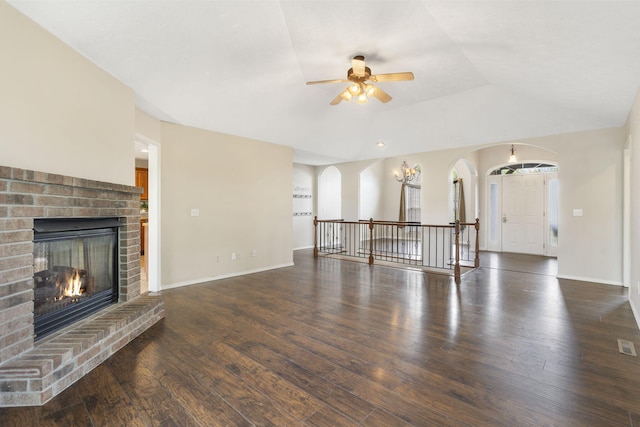 unfurnished living room featuring baseboards, arched walkways, a fireplace, wood finished floors, and a ceiling fan