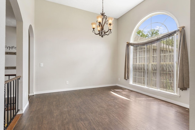 empty room with baseboards, arched walkways, a notable chandelier, and dark wood-type flooring
