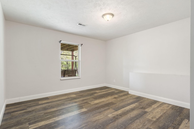 empty room featuring a textured ceiling, visible vents, dark wood finished floors, and baseboards